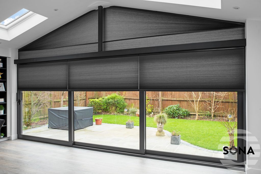 Black pleated blinds on triangular gable window and sliding glass doors overlooking landscaped garden patio.
