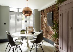 Dining room with tulip marble table, Eames chairs, copper pendant light, and exposed brick accent wall.