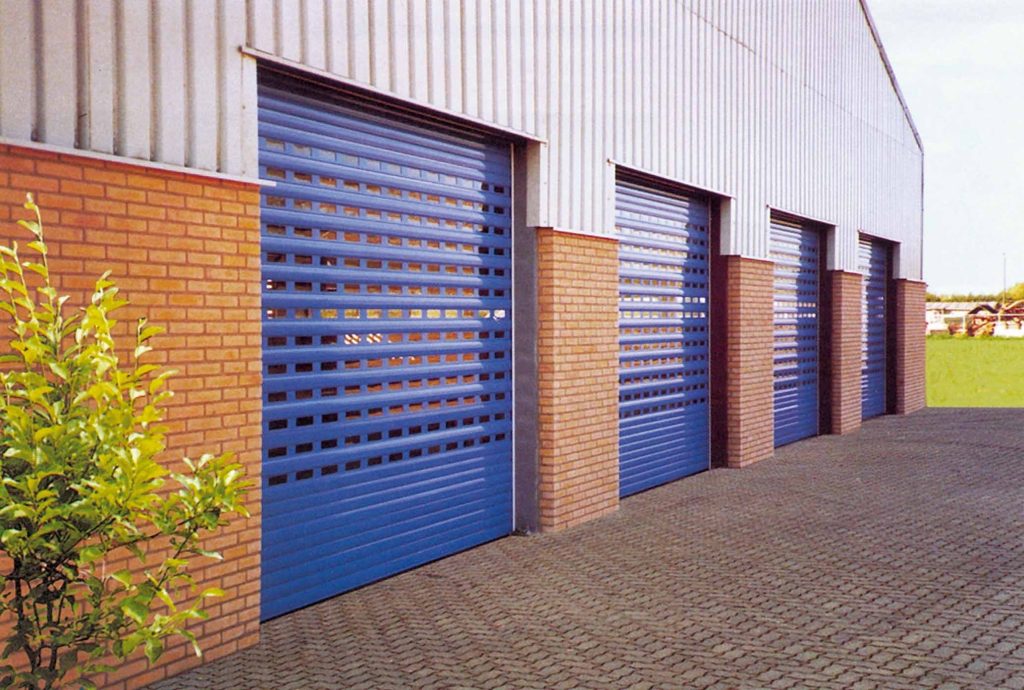 Industrial warehouse with brick walls and multiple blue perforated roller shutter doors along the exterior facade.