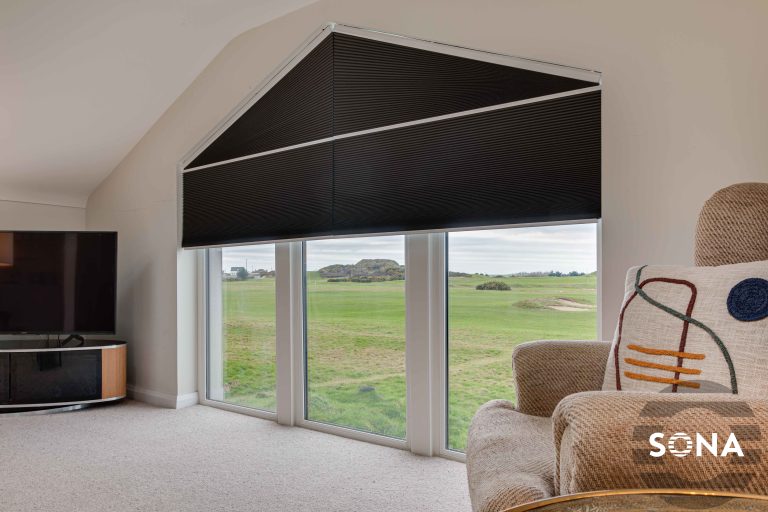 Custom-shaped black cellular blinds on triangular window overlooking golf course, in living room with cozy armchairs.