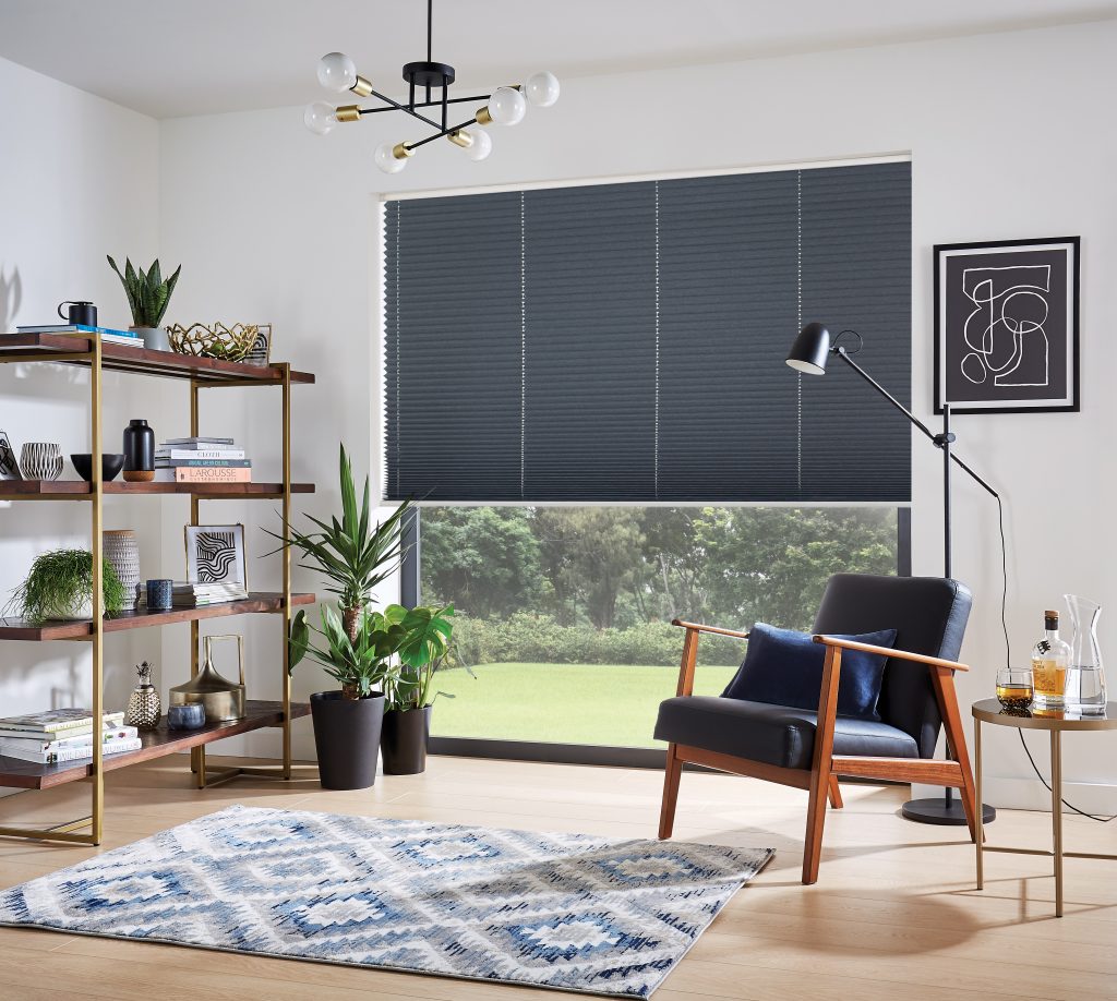 Modern living room with navy blue accent chair, gold-framed bookshelf, patterned rug, and pleated shade window covering.