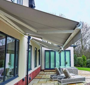 Retractable patio awnings extended over outdoor patio with rattan furniture, dining set, and bi-fold doors on modern home