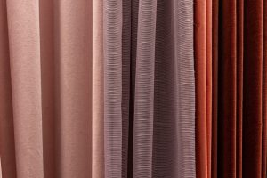 Different curtain fabric samples in pink, mauve, coral, and rust tones showing textured drapery folds.