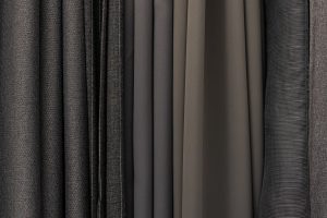 Assorted dark fabric swatches in gray and black tones, showing woven, ribbed, and smooth textile textures side by side.