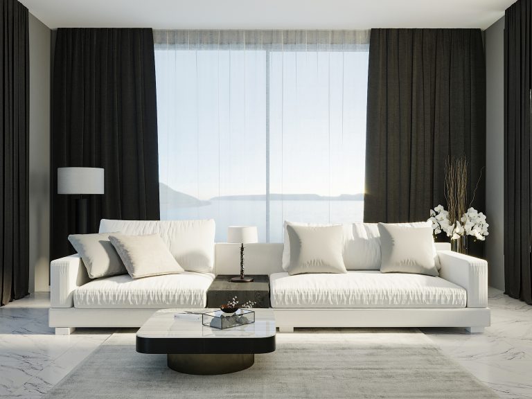 Modern living room with white sofa, dark curtains, marble coffee table, and ocean view through floor-to-ceiling windows.