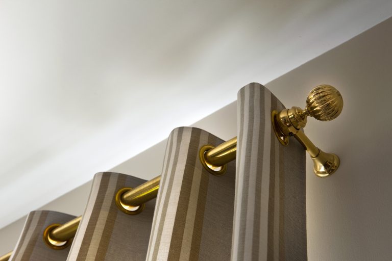 Striped curtain with brass grommets hanging on a gold curtain rod with decorative finial against a white wall