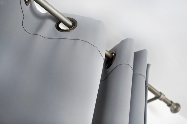 Close-up of gray grommet-top curtains hanging on a metal rod, showing fabric folds and stitching detail.