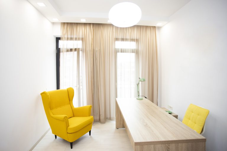 Bright office with yellow wingback chair, wooden desk, mint lamp, beige curtains, and round pendant light fixture.